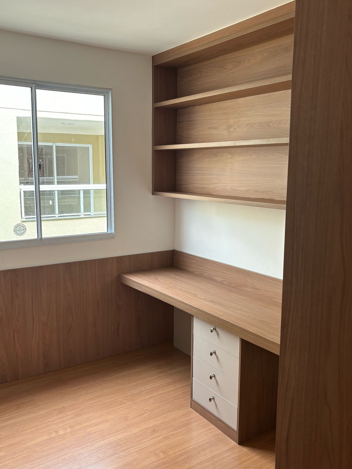 Escritório planejado com mesa em L, gaveteiro branco, prateleiras superiores em MDF amadeirado e meia-parede revestida